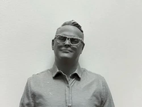 Close-up of a 3D printed portrait figure with glasses, straight off the printer before finishing
