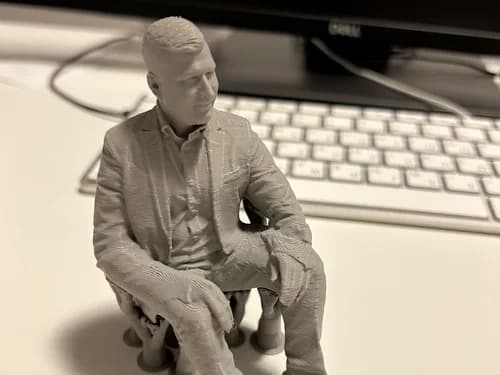 Desk-size 3D printed seated figure of a man in a suit, sculpted from photos and shown unpainted